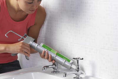 Woman applying sealant between a wall and a sink