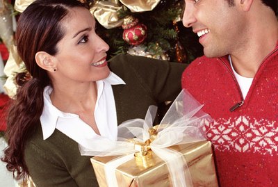 Woman handing man gift at dinner table by christmas tree