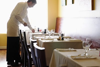Young man setting tables in restaurant, side view