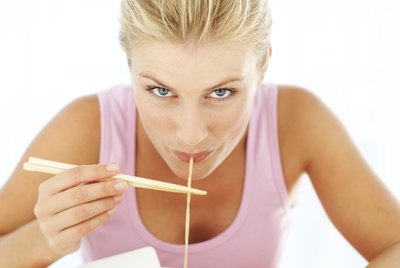 woman eating noodles from a take-out box with chopsticks