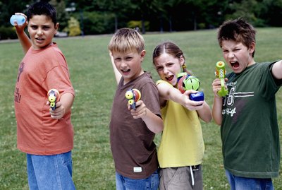 Children (9-12) in park aiming water pistols and water bombs, portrait