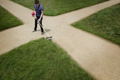 Man standing on dirt crossroad trimming lawn