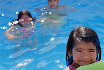 Boy (12-14) and two girls (4-7) swimming in pool (selective focus)