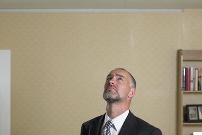 Mature man in suit with clipboard looking up at crack in ceiling