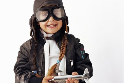 Girl (3-5) wearing goggles holding toy aeroplane, smiling, portrait