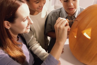 Mother carving a pumpkin with her son and daughter