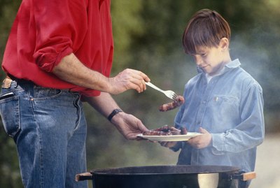 Father serving cooked food in son's (6-9) plate, outdoors