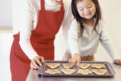 Young Girl Stands With Her Mum by the Kitchen Counter, Choosing a Christmas Cookie From a Baking Tray