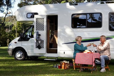 Mature couple having picnic by motor home in park, toasting