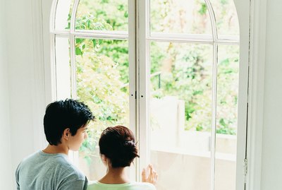 Young Couple Stand Looking Through French Windows Into Garden