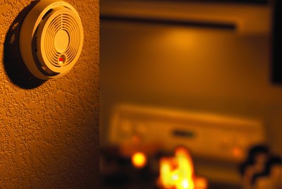 An off-centered view of a smoke detector, a small kitchen fire is in the background