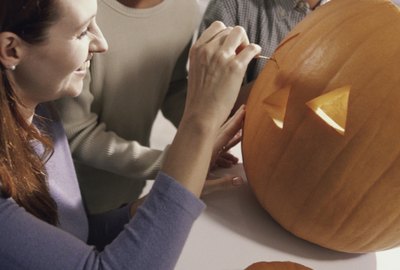 Mother carving a pumpkin with her son and daughter