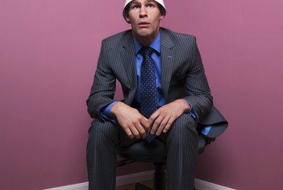 Businessman sat in corner wearing dunce hat