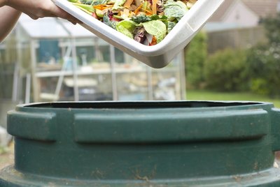 Unrecognizable person pouring kitchen waste into compost bin, close-up of hands