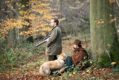 Couple in forest with shotgun and dog, side view