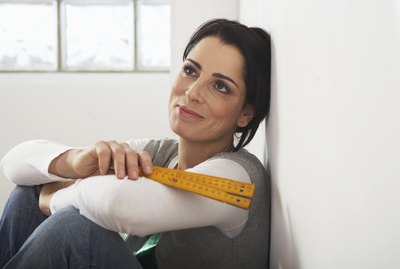 Woman leaning against wall holding measuring tape