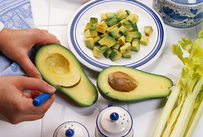close-up of hands scooping the flesh from an avocado on a tiled counter