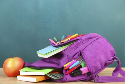 Purple backpack with school supplies on table of desk background