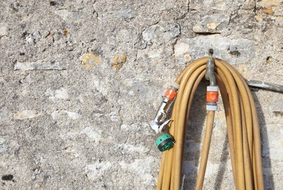 Coiled garden hose hanging on faucet against stone wall