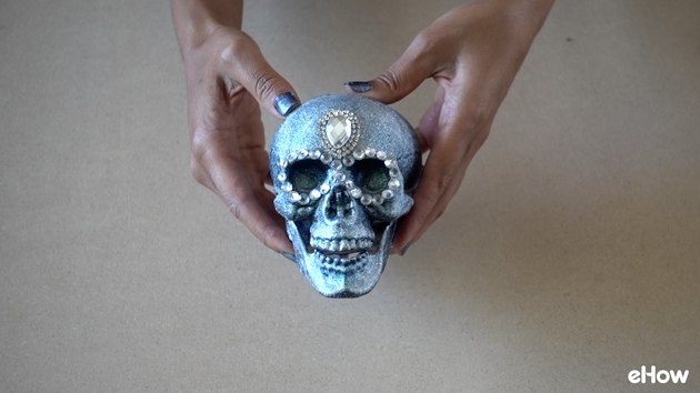 Applying gemstone strip around eyes of plastic skull for DIY Gemstone Studded Halloween Skull