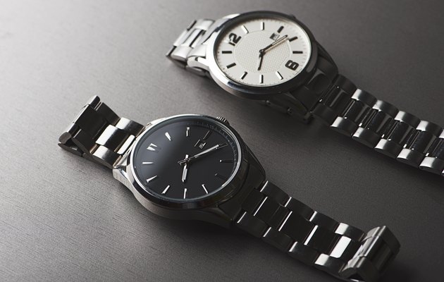 Two metallic wristwatches on gray background. Horizontal studio shot.