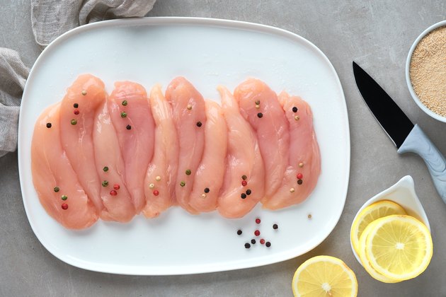 Raw chicken fillet. Meat with breadcrumbs, herbs , lemon and cooking oil. Top view on light colored stone