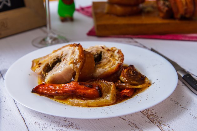 Sliced pork roll with vegetables on a white plate side view. Porketta