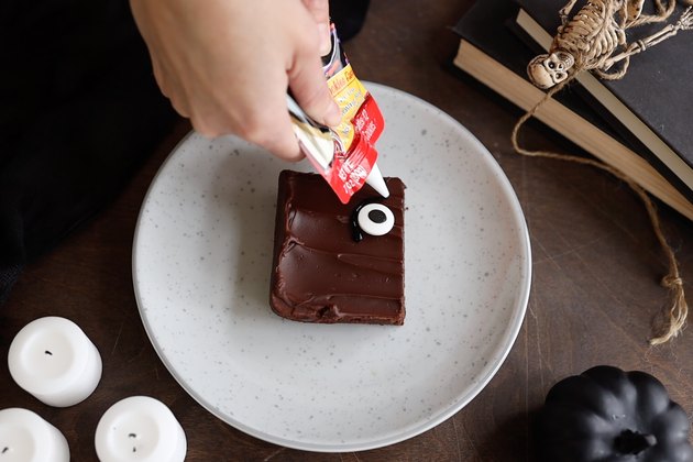 Piping black icing around candy eye on brownie