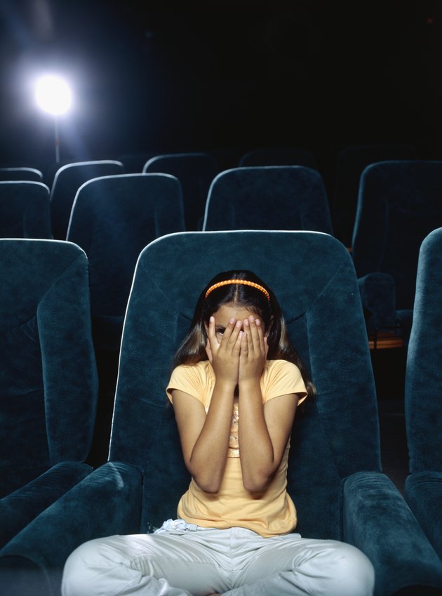 Girl covering her face with her hands in a movie theatre