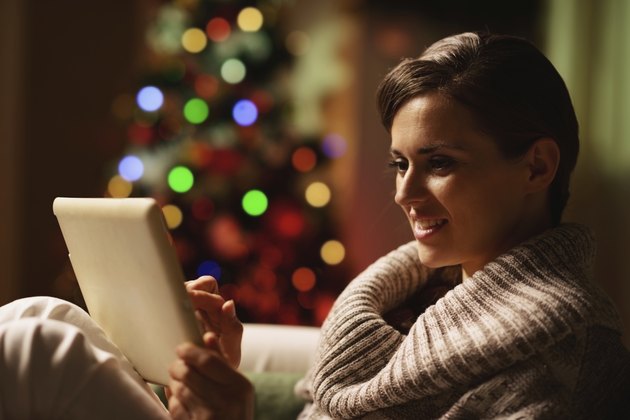 Happy woman using tablet pc in front of christmas tree
