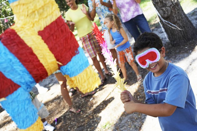 Boy (6-8) hitting pinata in garden, family in background