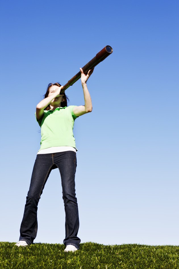 Cute brunette in field looks through antique telescope