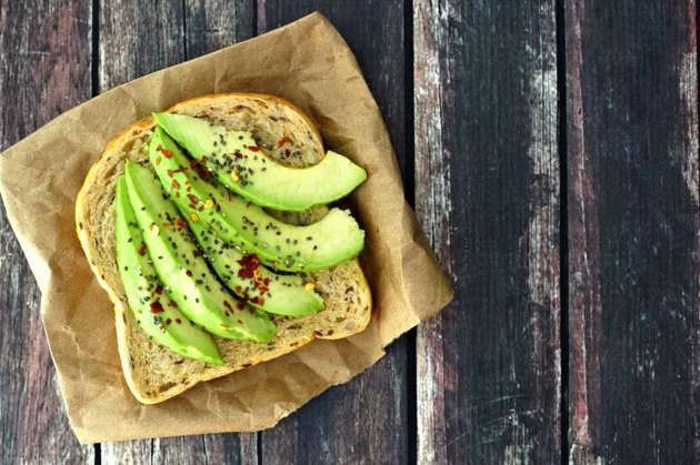 Open avocado sandwich with whole grain bread on paper against a rustic wooden background