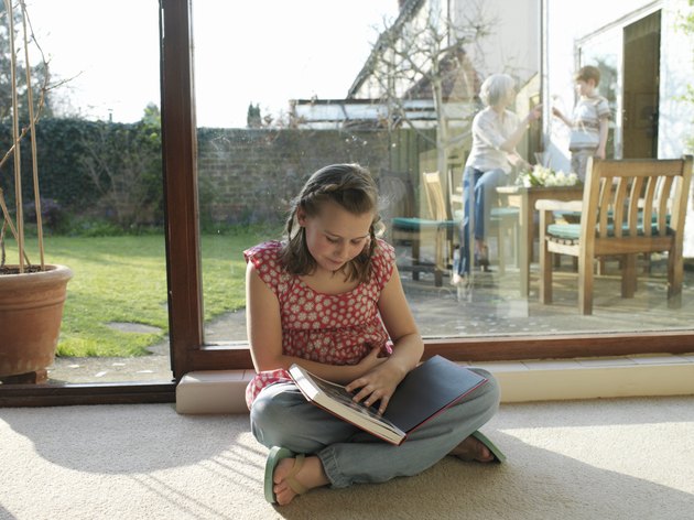 Girl (9-11) sitting on floor looking at photo album