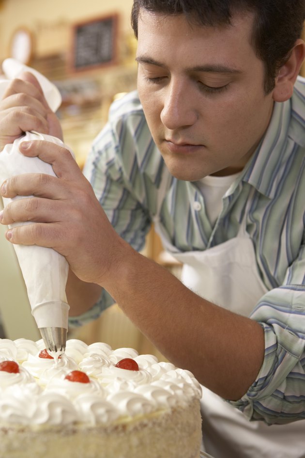 Young man wearing apron, putting whipped cream on cake