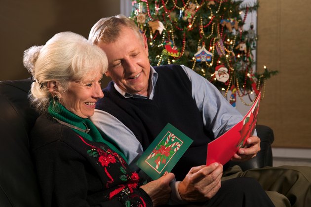 A mature couple enjoy and share Christmas cards near their decorated tree.