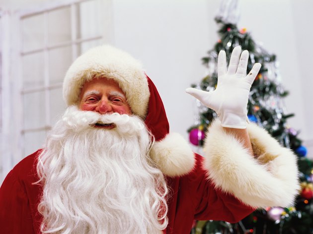 Father Christmas standing with arms up, smiling, portrait, Christmas tree in background
