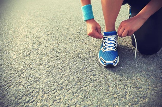 young woman runner tying shoelaces on city road