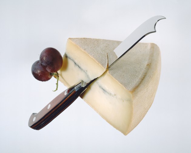 Slice of cheese, grape and knife on white background, close-up