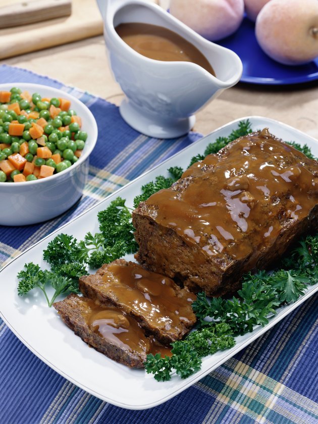 Meatloaf, gravy, mixed vegetables, and bread sitting on a table