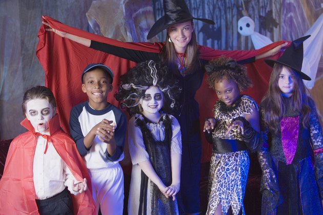 Woman spreading cape around children in Halloween costumes