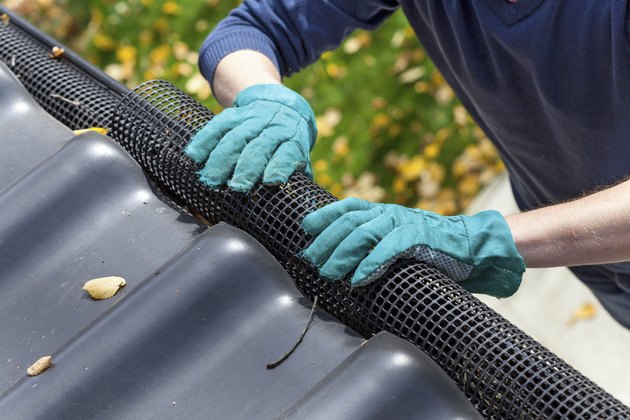 Man's hands in gloves securing gutters with a black net