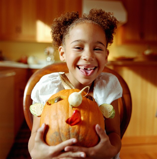 Girl (6-8) holding decorated pumpkin, smiling, portrait