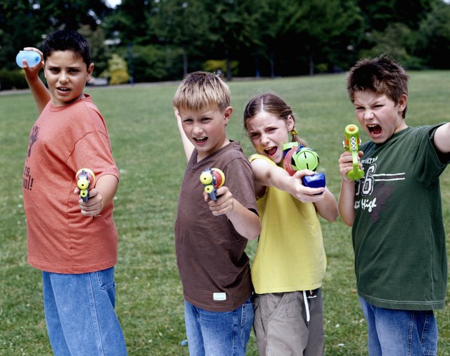Children (9-12) in park aiming water pistols and water bombs, portrait