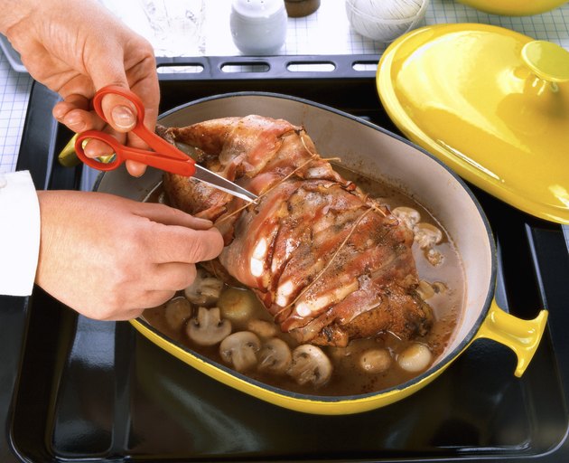 close-up of hands snipping thread off a chicken pot roast bound with bacon slices