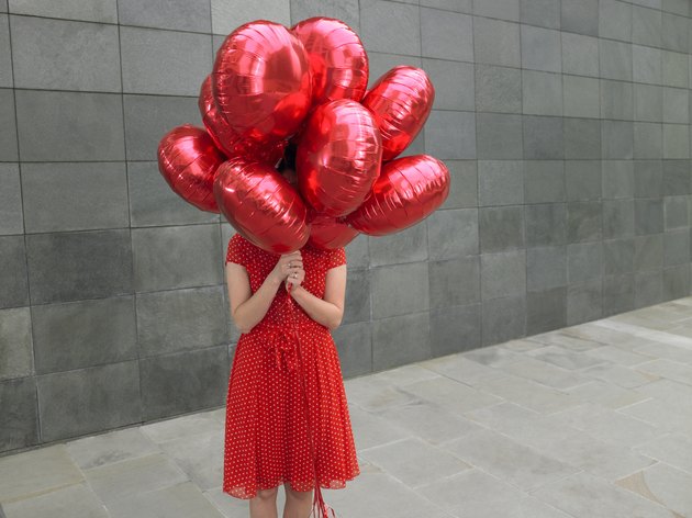 Young woman holding bunch of red foil balloons, face obscured