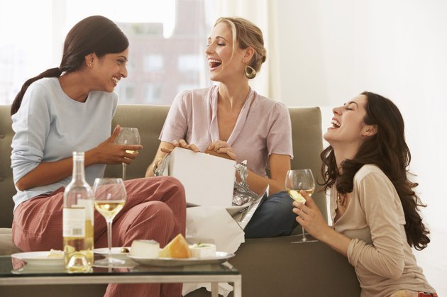 Three young women gathered on sofa, drinking wine and laughing