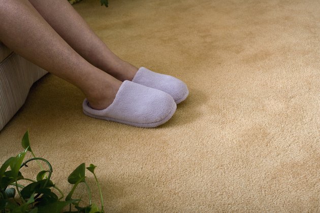 Mature woman sitting wearing slippers, low section, close-up of legs, feet and carpet