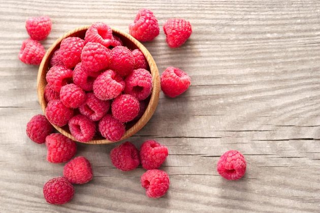 Ripe sweet raspberries in bowl on wooden table. Close up, top view, high resolution product
