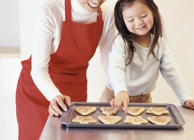 Young Girl Stands With Her Mum by the Kitchen Counter, Choosing a Christmas Cookie From a Baking Tray